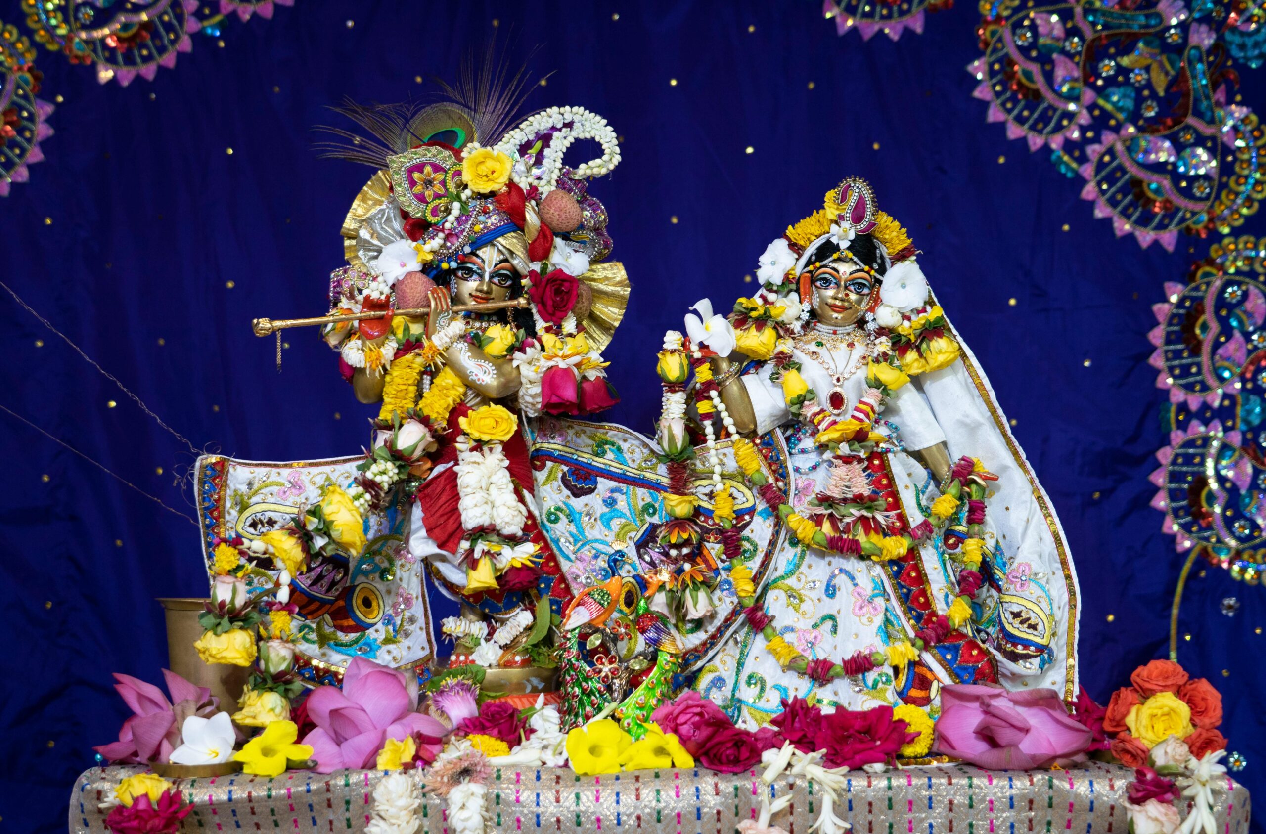 Vibrant sculptures of Indian deities adorned with flowers on a blue background.